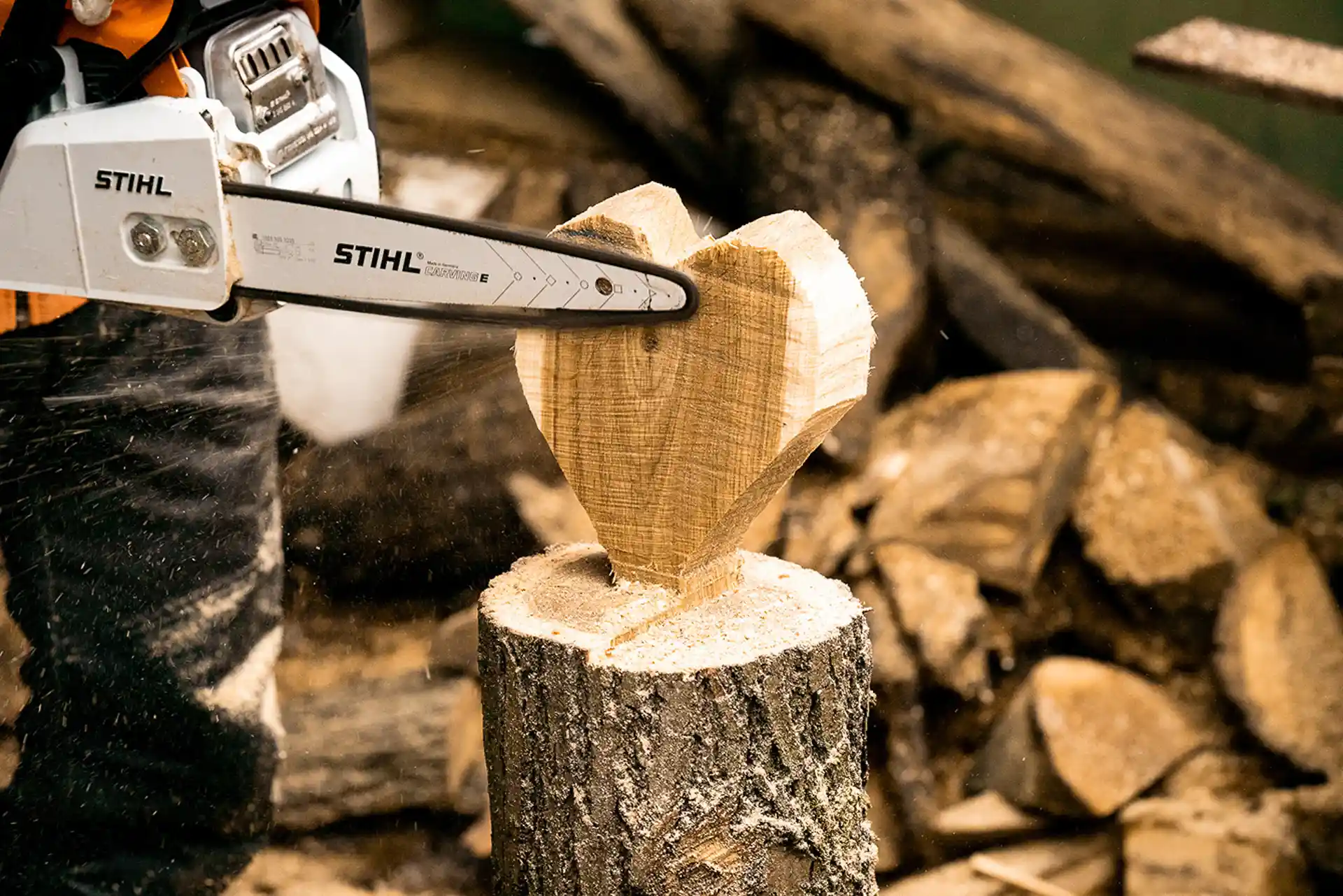 Na drewnianym stole znajdują się różne modele pilarek spalinowych Stihl, w tym pilarki łańcuchowe i pilarki spalinowe, które są idealne do cięcia drewna opałowego oraz przycinania gałęzi. Każdy model charakteryzuje się ergonomiczną konstrukcją i systemem antywibracyjnym, co zwiększa komfort pracy.